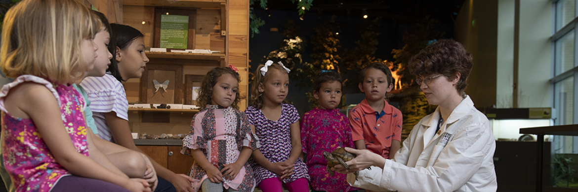 Science Center image showing a tour guide presenting a turtle to a group of children